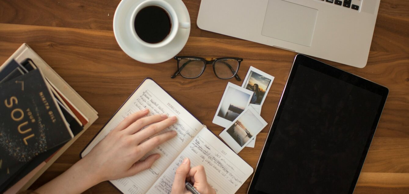 person holding ballpoint pen writing on notebook
